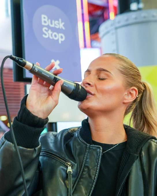 Person singing into a microphone at a Busk Stop located in Xscape in Castleford, Yorkshire