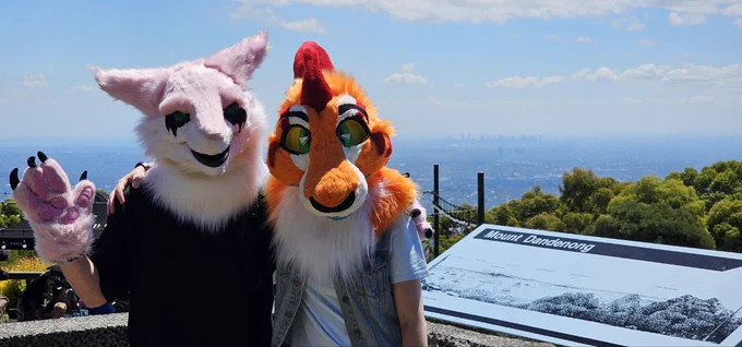 Two fursuiters standing together posing for a photo infront of the Melbourne skyline