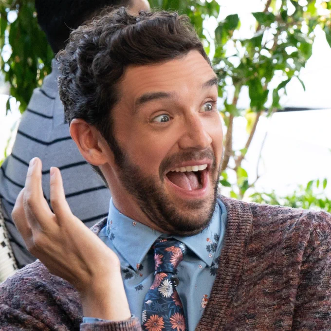 From Shrinking. Michael Urie as Brian smiles with his hand raised near his face, wearing an expression of pure glee on his face.