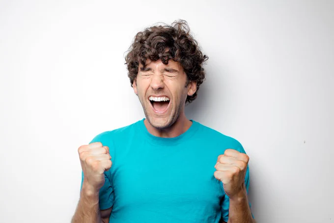 Portrait of a joyful man in a blue shirt celebrating with excitement and closed eyes.
