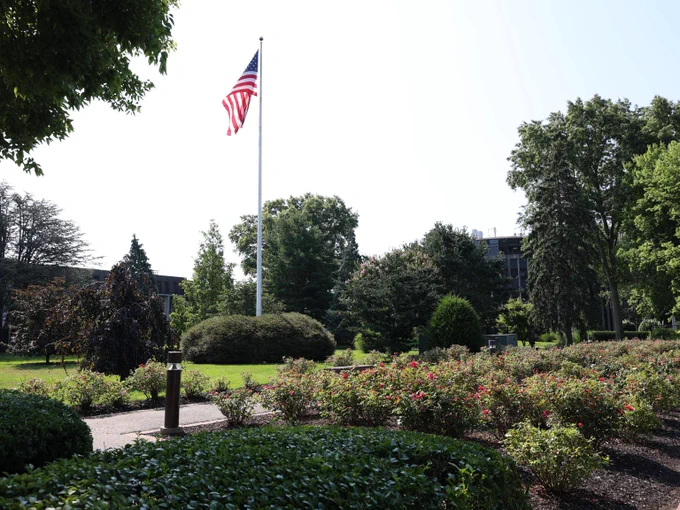 Campus in summer, rose garden just starting to bloom, flag in the background