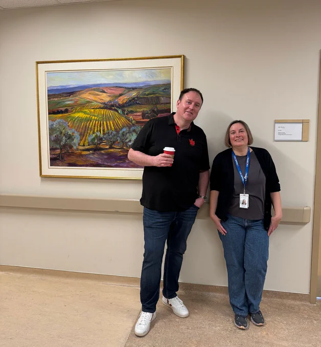 ArtWorks for Cancer team member Alan Loch of Loch Galleries (left) and Patricia Mosnia, Clinical Director – Oncology and Palliative, Brampton Civic Hospital (right) pause to drink in the work Tuscan Morning by Joanne Clarke in the Inpatient Oncology/Palliative Care Unit.