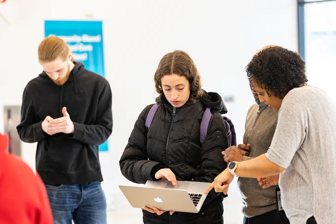 Three people on campus looking at a laptop together, with one person pointing at the screen.