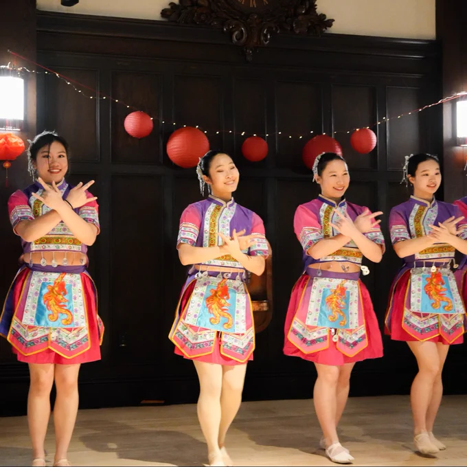 Four dancers in traditional attire performing at an indoor event decorated with red lanterns.