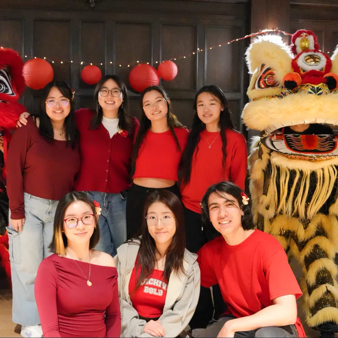 Eight individuals in red shirts posing with traditional Chinese lion dance costumes during a celebration event.