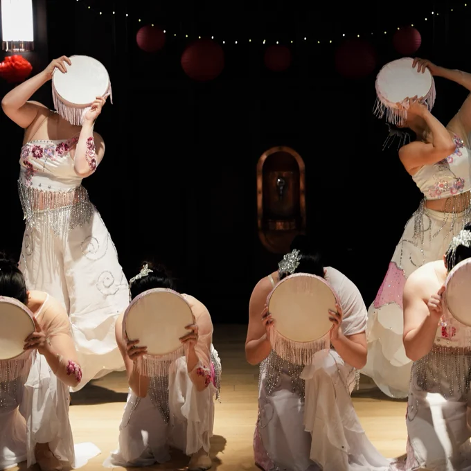 Performers in traditional costumes with drums bowing on stage, with hanging red lanterns in the background.