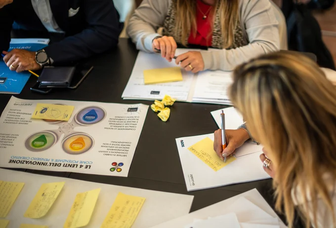 a photograph of people working at a desk with papers and post-it notes, writing down ideas 