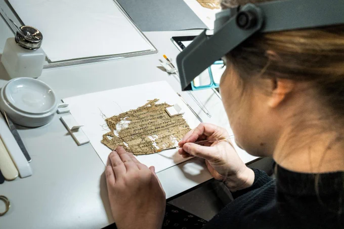 A begoggled conservator working on a delicate piece of papyrus