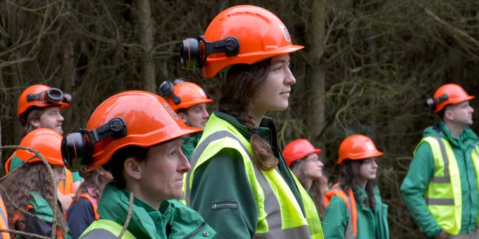 Apprentices in high-vis and hard hats in a woodland.