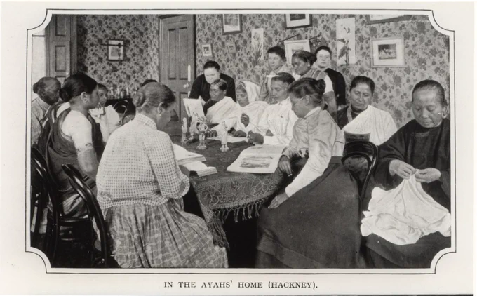 Black and white photo of the Ayahs' Home in Hackney, showing a number of women sitting around a table, reading and embroidering.