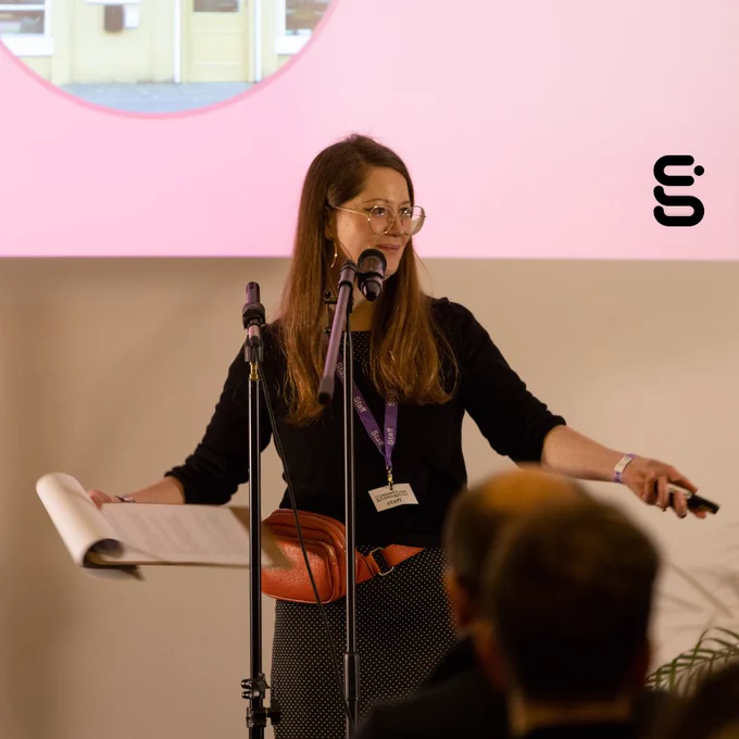 A presenter stands on stage behind a microphone.