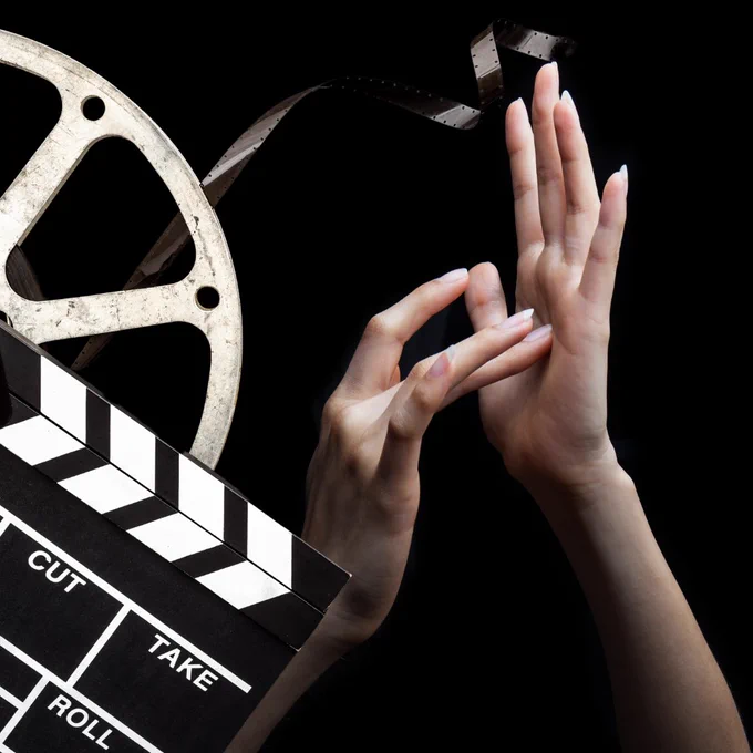 A film reel and clapperboard with a person's hands signing in American Sign Language against a black background.