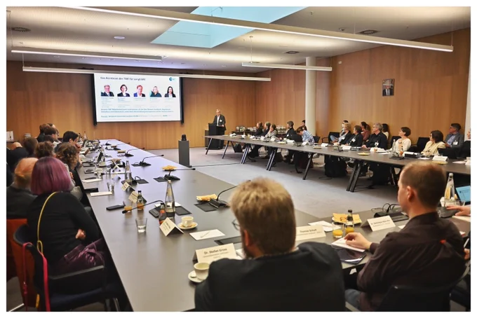 ein Mann steht vor einer Gruppe von Menschen, die an langen Tischen sitzen.