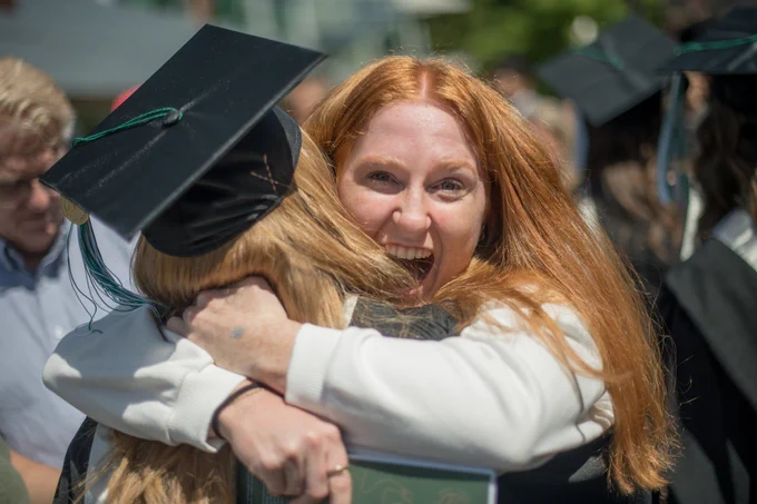 A woman hugs a graduate wearing a cap and gown.