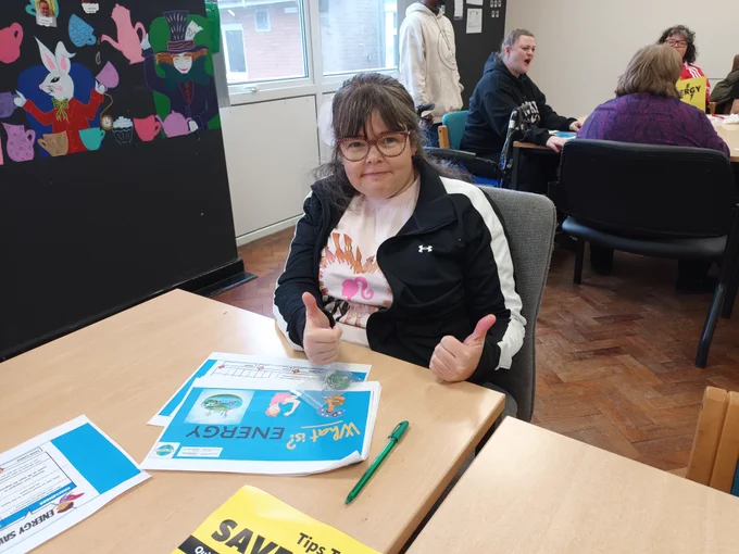 Individual sitting at a table with the energy workbook in front of her. She is smiling and has her thumbs up.