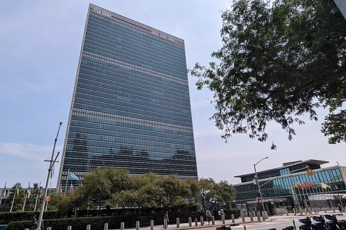 An image of the UN Headquarters in New York, which is a tall skyscraper made from blue reflective material.