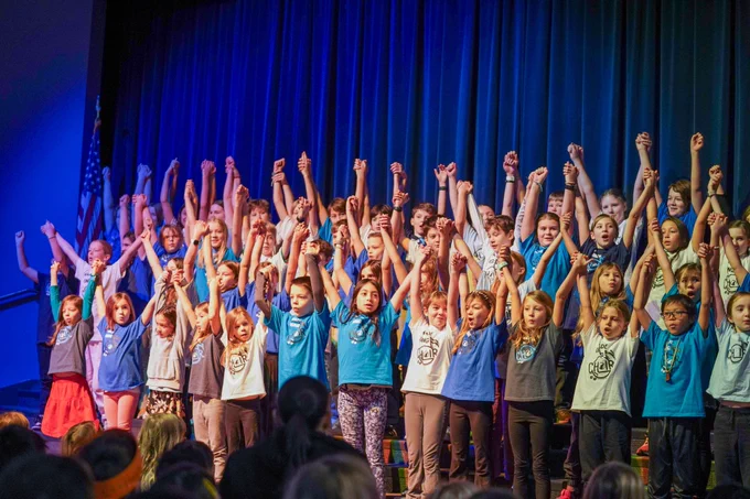 The 2024-25 Wade King morning choir performs during the school's Martin Luther King Jr. Day assembly with hands raised on stage.