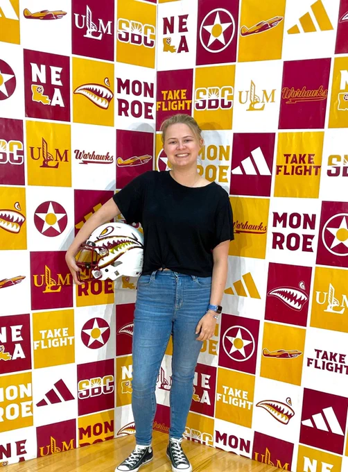a person stands in front of a step and repeat background holding a football helmet