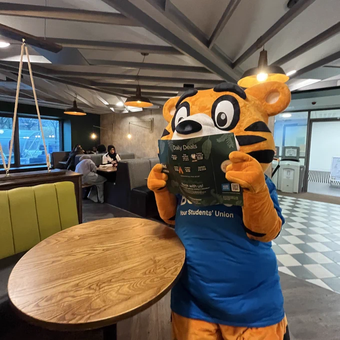 Tiger mascot in cafe with menu over their face