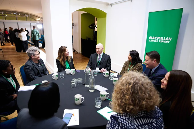 A group of people sat around a table at an event with a Macmillan Cancer Support banner. People around the table include, Secretary of State for Health and Social Care, Wes Streeting, Macmillan Chief Executive, Gemma Peters and Cancer Minister, Ashley Dalton.