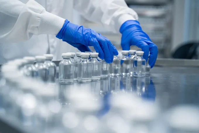 Detail of hands working in pharmaceutical factory handling sterile bottles.