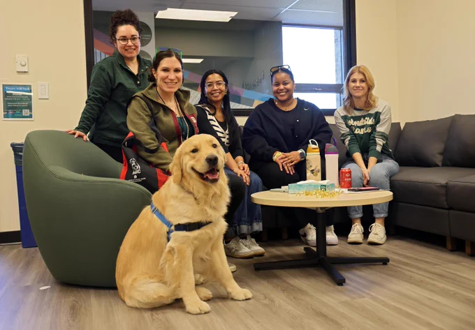 Graduate students, a Dean, and a dog sit on a couch smiling