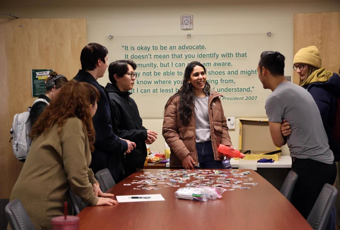 Graduate students stand around a table chatting.