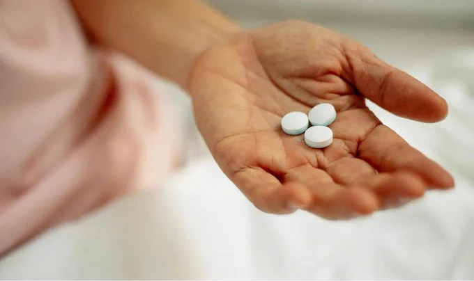 A close-up image of someone holding three white tablets in their hand.