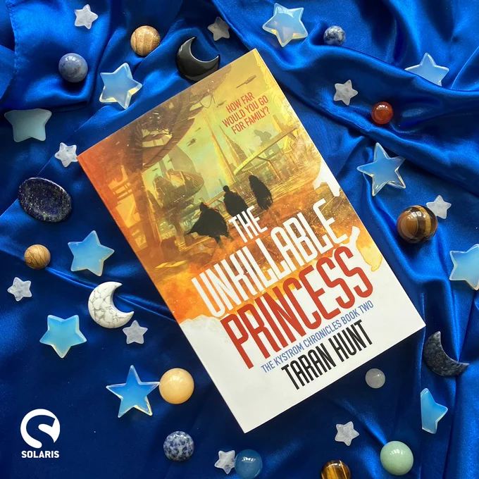 Against a blue fabric background dotted with crystal plants, stars and moons, a flatlaid paperback copy of THE UNKILLABLE PRINCESS by Taran Hunt. The white Solaris logo is in the bottom left corner.