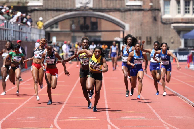 photo of five sets of relay runners on a track, all Black women in different countries' colors, passing their batons