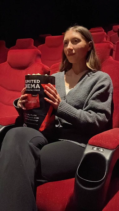 Person holding popcorn while sitting in a theater with red seats.