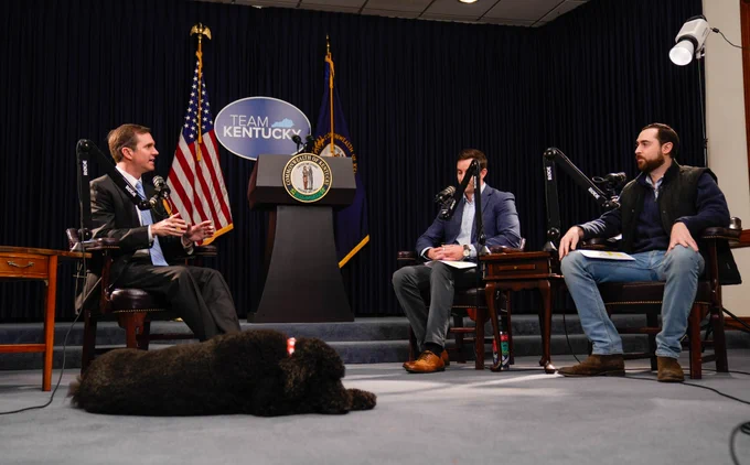 An image of Governor Beshear speaking with the hosts of Middle Tech Podcast. First Dog Winnie naps in the foreground.