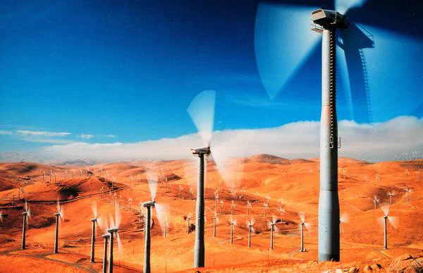 Credit: Department of Energy, public domain. Field of wind power turbines used to produce energy, blue sky, clouds in background.