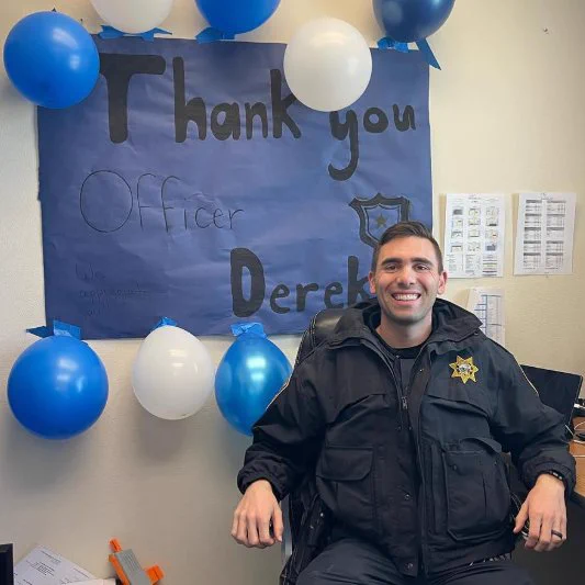 Photo of a School Resources Officer named Derek, sitting in a chair and smiling at the camera. Credit @NASRO_Info