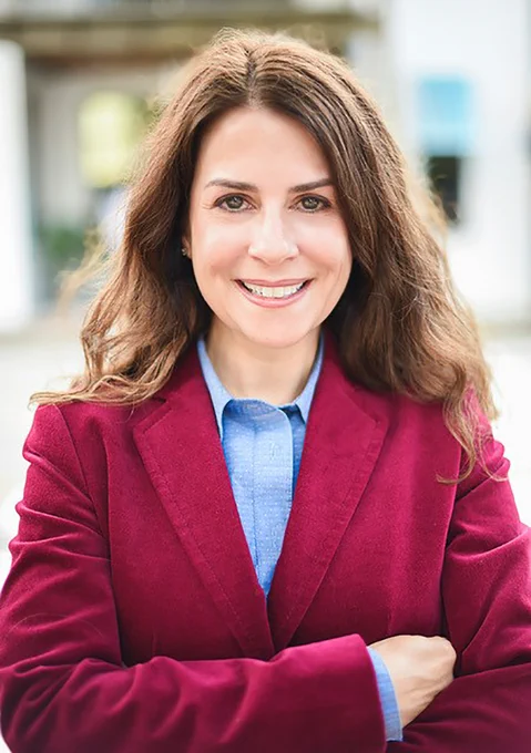 Speaker and author Amanda VanDerHayden, smiling, wearing a red blazer and blue shirt, outdoors.