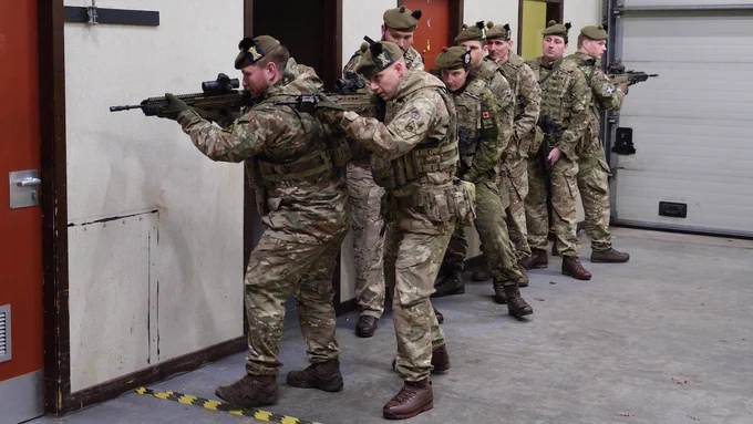 Eight uniformed soldiers training with weapons in a hallway.