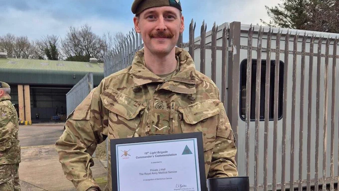 A uniformed soldier holding a certificate and an award.