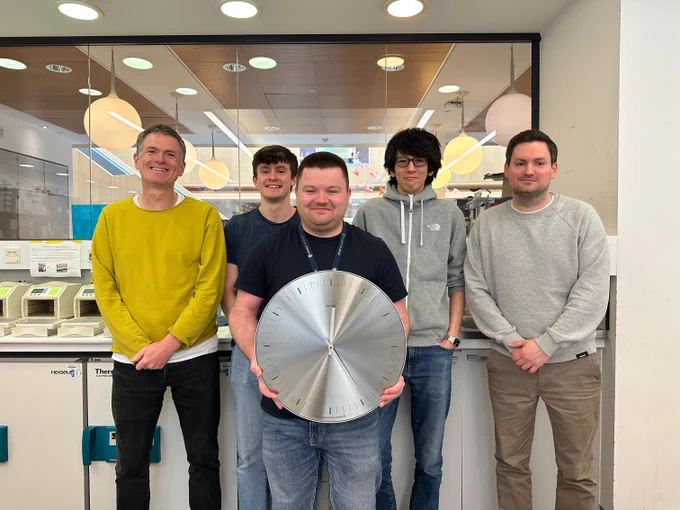 Five members of the Barr lab stand in a row with the middle person standing in the foreground and holding a clock to illustrate the story.