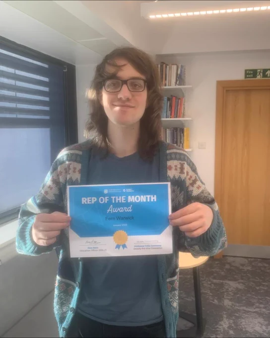 Image of a student smiling at the camera whilst holding up a certificate for Rep of the Month.