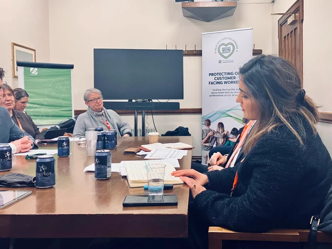 Maryam Eslamdoust sits on the right of the picture, speaking at a table with parliamentarians and campaigners sitting on the the left. In the background is a white banner which says "protecting our customer-facing workers".
