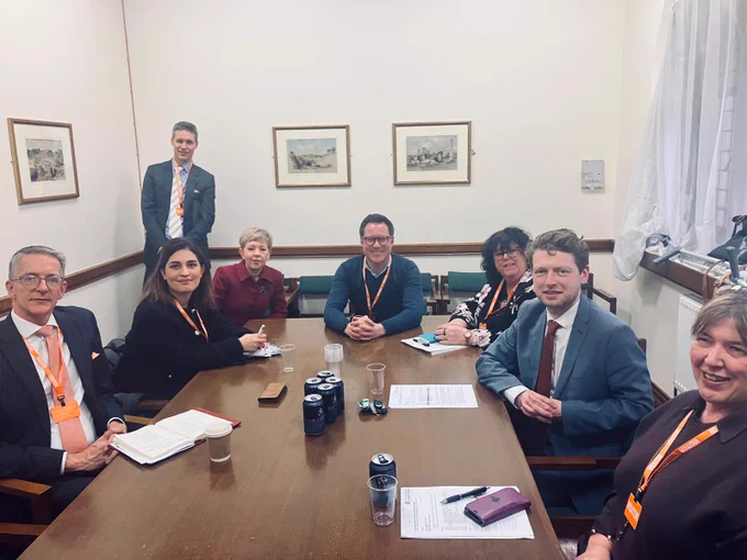 A group of parliamentarians, business representatives, trade unionists, and campaigners sitting around a rectangular table. All are looking at the camera.