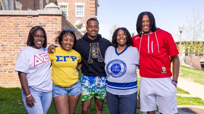 Lincoln University of Missouri students smiling and walking arm-in-arm near campus residential halls on a spring day.
