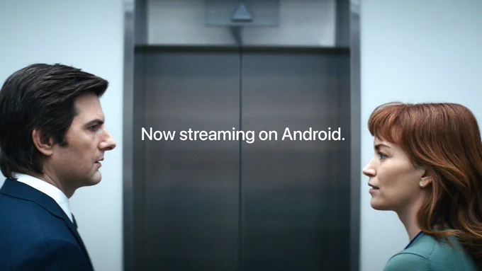 From Severance. Mark, portrayed by Adam Scott, is facing Helly, portrayed by Britt Lower. They are staring at one another blankly with an elevator in between them. There is text on-screen that reads "Now streaming on Android."