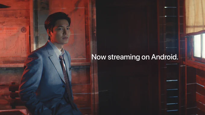 From Pachinko. Koh Han-soo, portrayed by Lee Min-ho, looks dapper in a silver suit. There is text on-screen that reads "Now streaming on Android."