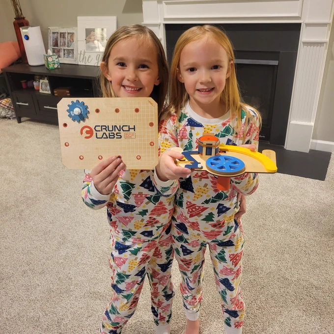 Two children in pajamas smiling and holding CrunchLabs toys in a living room.