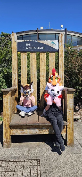 Three fursuiters sitting on a giant chair