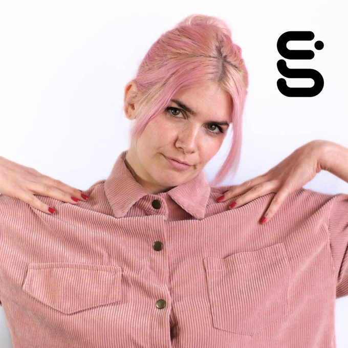 A portrait of Kate Hammer wearing a pink shirt with pink hair and red nails.