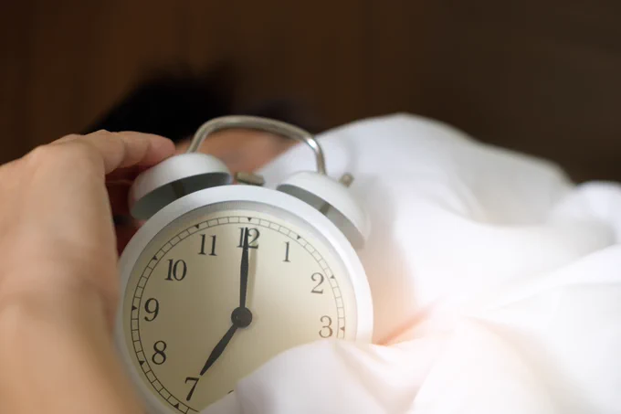 person in bed, holding an alarm clock