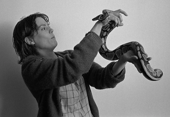 A black and white image of a woman holding a snack and looking at it straight in the eyes.