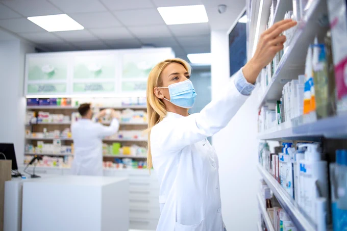 Image of a woman working in a pharmacy wearing a face mask. 